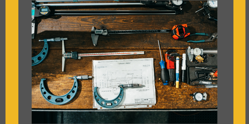 Mechanical engineering tools on wooden desk with small turning print blueprint by M&M International